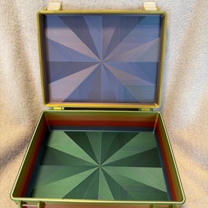 May include: A rectangular storage case with a hinged lid, featuring a vibrant rainbow gradient on the exterior sides. The interior base and lid display a geometric starburst pattern in shades of blue, green, and purple, with a metallic finish.
