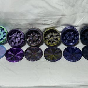 May include: A collection of colorful, cylindrical containers with matching lids. The containers are in various shades of blue, purple, and green. Each container has a unique interior design with multiple circular indentations. The lids feature a radial pattern.