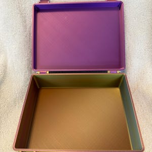 May include: An open, rectangular case with a purple interior and a gold-colored exterior. The case has a hinged lid and a clasp closure. The interior is a solid purple color, while the exterior is a metallic gold color.