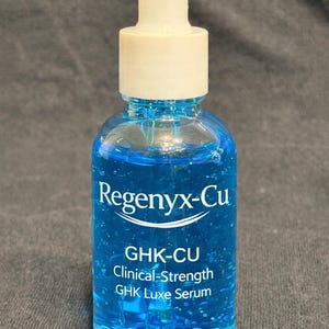 May include: A clear glass bottle filled with a vibrant blue liquid, featuring a white dropper top. The bottle is labeled "Regenyx-Cu GHK-CU Clinical-Strength GHK Luxe Serum". The bottle contains 30ml / 1.01 fl oz of serum.