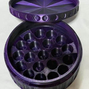 May include: A purple, round container with a removable lid. The lid has a geometric design and the container has multiple circular compartments. The container is made of a textured material.