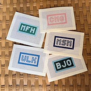 May include: Four rectangular needlepoint canvases featuring stitched monograms in coloured frames. The designs include the letters MFH in green, cno in red, MSM in dark blue, WLK in blue, and BJO in dark green, all on a white grid mesh background.