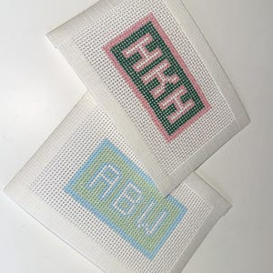 May include: Two needlepoint canvases with personalized initials. One canvas features the initials "HHH" in green and pink, while the other displays "ABW" in blue and green. Both are set against a white background.