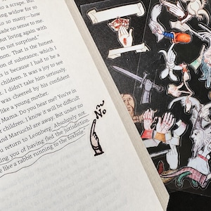 May include: A book page with printed text and a small hand illustration pointing to the word No, next to a sheet of clear stickers featuring various medieval-style illustrations of hands, swords, and bearded figures on a black background.