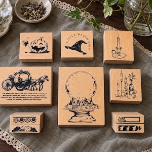 May include: A collection of eight wooden rubber stamps featuring black ink illustrations of a jack-o'-lantern, a witch hat with the text Little Witch Post, a candle, a horse-drawn carriage, a crystal ball, a candelabra, and two decorative borders.