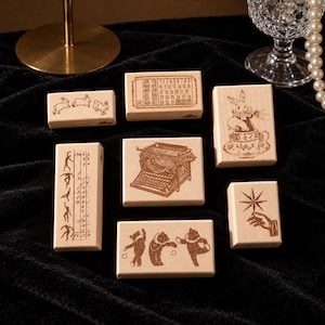 May include: A collection of seven rectangular wooden rubber stamps featuring detailed brown ink illustrations. Designs include a calendar, a typewriter, a rabbit in a teacup, dancing bears, jumping rabbits, a hand holding a star, and a figure chart.