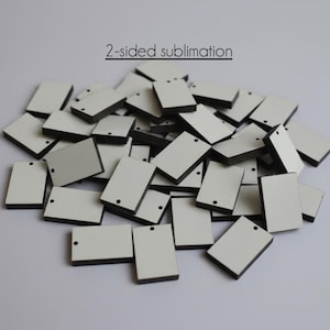 May include: A pile of rectangular sublimation blanks with white surfaces and black edges. Each blank has a small hole at the top for attaching a chain or cord. The text "2-sided sublimation" is above the pile.