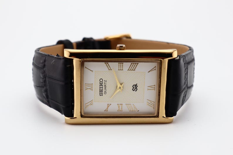 Puede incluir: Reloj Seiko Quartz dorado con esfera rectangular y correa de cuero negro. La esfera es blanca con n&uacute;meros romanos y agujas doradas. La correa tiene un patr&oacute;n de cocodrilo.
