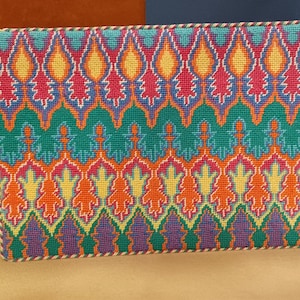 May include: A colorful needlepoint pillow with a geometric pattern in shades of orange, yellow, green, blue, and purple. The pillow has a decorative border.