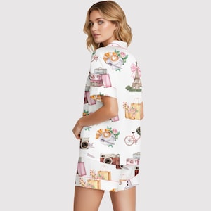 Puede incluir: Conjunto de pijama blanco con un estampado repetido de ilustraciones parisinas. El dise&ntilde;o incluye la Torre Eiffel, c&aacute;maras, cruasanes, tazas de caf&eacute;, bolsas de la compra y maletas. El conjunto tiene ribetes rosas.