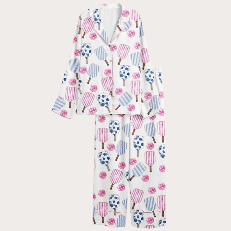 Może przedstawiać: Biały zestaw piżamowy z powtarzającym się wzorem r&oacute;żowych i niebieskich wzor&oacute;w w kształcie lod&oacute;w na patyku oraz r&oacute;żowych kropek. Top z długim rękawem ma kołnierzyk i zapięcie na guziki. Pasujące spodnie mają luźny kr&oacute;j.