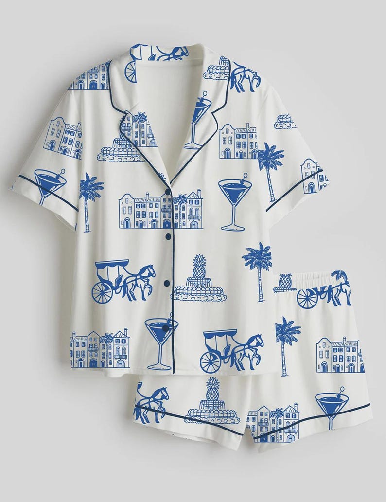 K&ouml;nnte beinhalten: Wei&szlig;es Pyjama-Set mit blauem Aufdruck von Geb&auml;uden, Palmen, Cocktails und Pferdekutschen. Das kurz&auml;rmelige Oberteil und die Shorts haben marineblaue Paspeln und Kn&ouml;pfe. Ein lustiges Schlafanzug-Set zum Thema Urlaub.