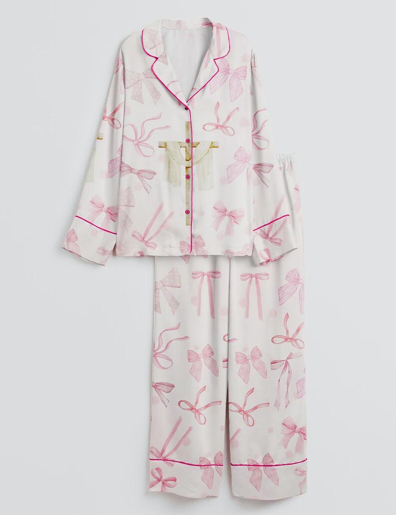 May include: White pajama set with a pink bow pattern. The long-sleeved top has a notched collar and pink trim. The matching pants have a straight leg and pink trim. The set is made of a soft, lightweight fabric.
