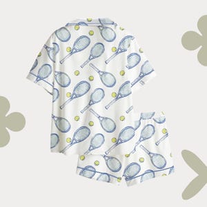 May include: White tennis-themed pajama set featuring a short-sleeved button-up shirt and matching shorts. The set is patterned with blue tennis rackets and yellow tennis balls. The edges of the shirt and shorts are trimmed with blue.
