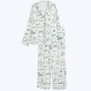 May include: White pajama set with a green St. Patrick's Day themed pattern. The set includes a button-down top and pants, both adorned with shamrocks, pots of gold, rainbows, and the word "lucky". The trim is green.