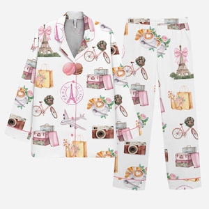 Puede incluir: Conjunto de pijama blanco con un patr&oacute;n repetido de elementos de viaje parisinos. El dise&ntilde;o incluye la Torre Eiffel, bicicletas rosas, maletas, c&aacute;maras, bolsas de la compra y la frase "Paris Je t'aime".