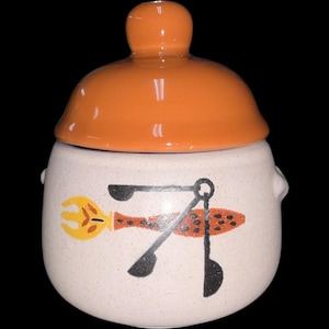 May include: A ceramic jar with a lid, featuring a speckled white body and an orange lid. The jar is decorated with a yellow fork, a red and orange fish, and black utensils. The jar has two small handles on the sides.