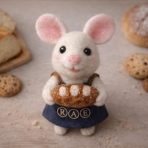 May include: A handcrafted felt mouse figurine, holding a loaf of bread. The mouse is white with pink ears and a pink nose, wearing a blue denim apron. The bread is brown with white dots. The apron has the letters "RAE".