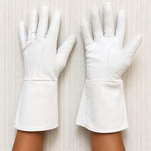 May include: A pair of white leather gloves featuring long, flared cuffs that extend past the wrist. The gloves have visible stitching details on the back of the hand and a smooth, matte finish, covering the fingers and palms completely.
