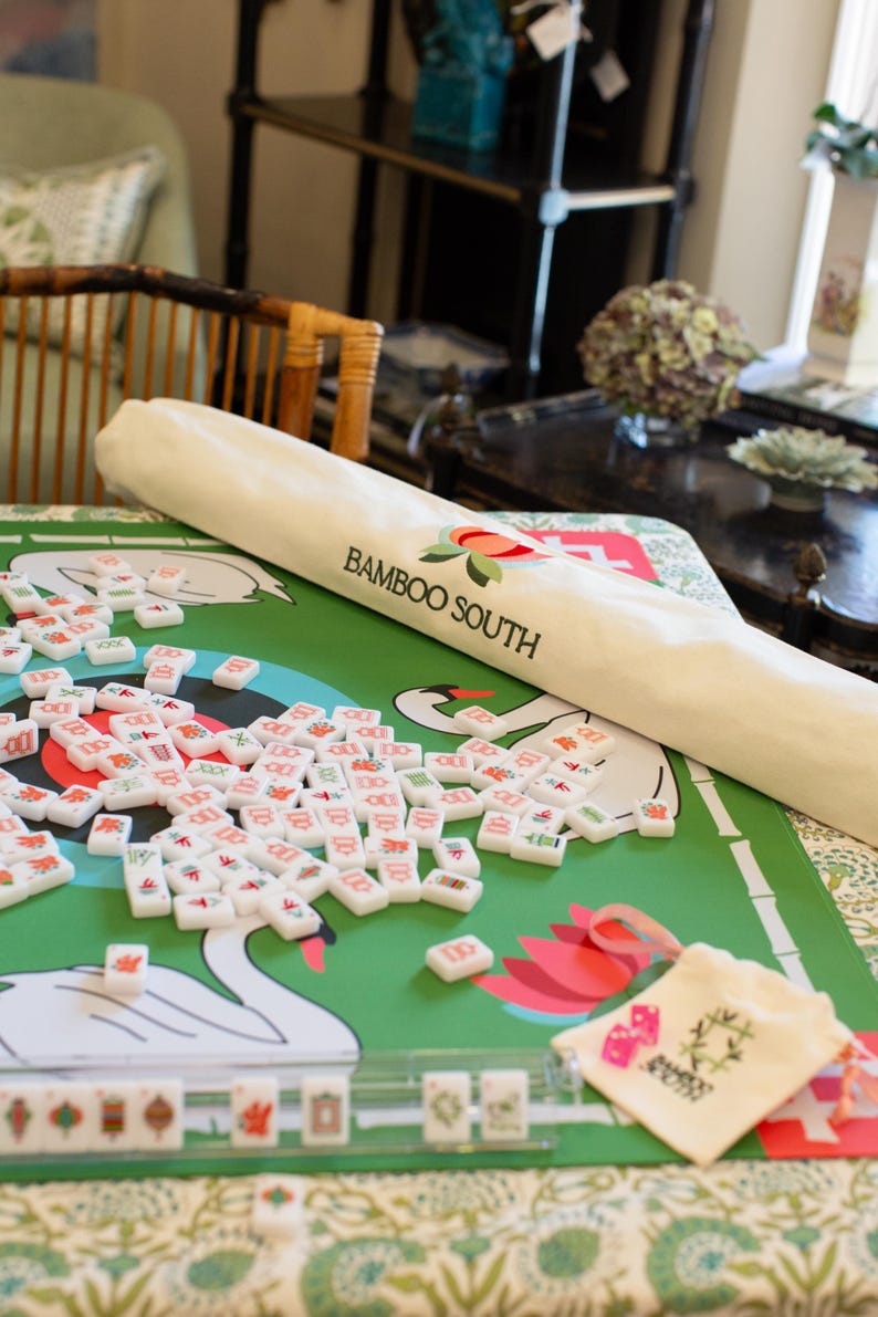 May include: A green mahjong game mat with a swan design and the text "Bamboo South". The image shows a set of mahjong tiles scattered on the mat, along with a matching carrying case and a rolled-up mat.