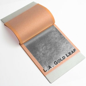 May include: A book of silver leaf with the text "L.A. Gold Leaf" printed on the cover.