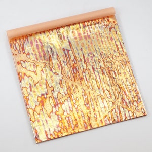 May include: A sheet of gold leaf with a textured, iridescent finish. The leaf has a warm, orange-gold color with hints of pink and silver. The leaf is rolled up and ready to be used for decorative purposes.