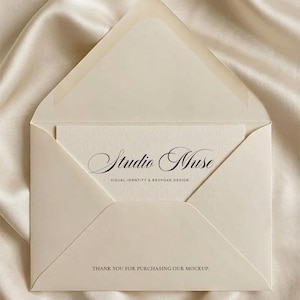 Puede incluir: Un sobre crema abierto, revelando una tarjeta a juego, sobre un fondo de satén. La tarjeta muestra el texto "Studio Muse" en una escritura elegante, con el lema "VISUAL IDENTITY & BESPOKE DESIGN" debajo. La parte inferior de la tarjeta dice "THANK YOU FOR PURCHASING OUR MOCKUP."