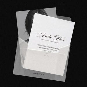 May include: A black and white image of stationery. A white card with the text "Studio Muse" and "Thank you for supporting our creative studio" is in a translucent envelope. The brand name "AMBRINN" is at the bottom.