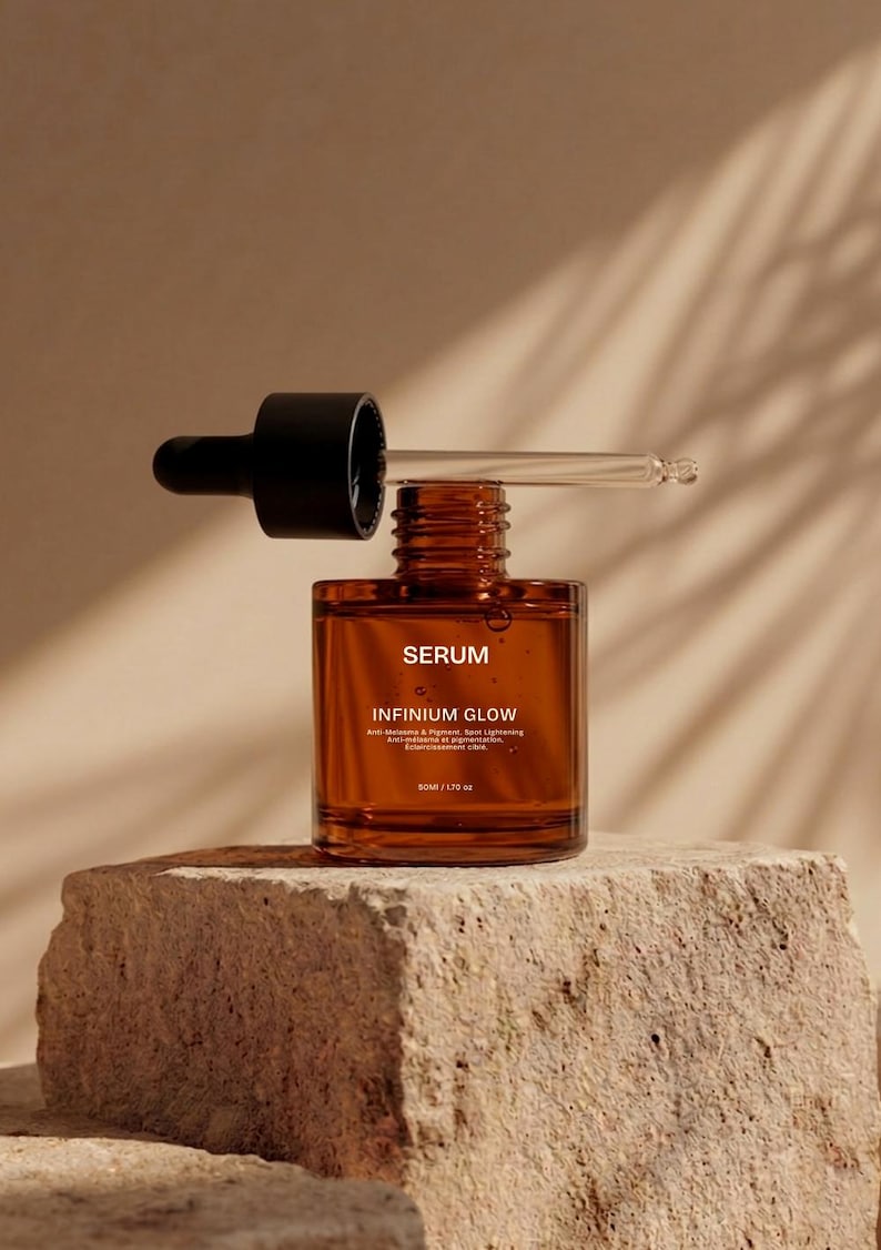 Puede incluir: Una botella de suero de vidrio marr&oacute;n con un cuentagotas negro, etiquetada como "SERUM" e "INFINIUM GLOW". La botella se encuentra sobre una superficie de piedra texturizada. El cuentagotas est&aacute; parcialmente insertado en la botella, con una pipeta de vidrio transparente.