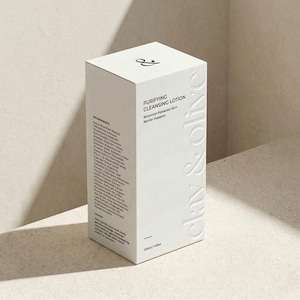 Op de afbeelding: Een witte doos met "Purifying Cleansing Lotion" van Clay & Olive. De doos heeft reliëftekst op de zijkant en het merklogo bovenop. De voorkant bevat ingrediënten en gebruiksaanwijzingen. Bevat 125 ml / 4 fl oz product.