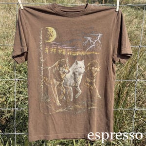 May include: Espresso-colored t-shirt featuring a graphic of three wolves running under a moonlit sky with lightning. The design includes a white wolf and two brown wolves. The word "espresso" is printed at the bottom.