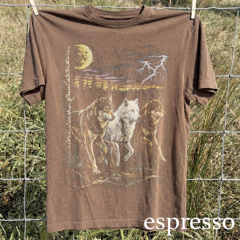 May include: Espresso-colored t-shirt featuring a graphic of three wolves running under a moonlit sky with lightning. The design includes a white wolf and two brown wolves. The word "espresso" is printed at the bottom.