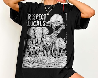 May include: A black t-shirt featuring a white graphic print of various African wildlife including an elephant, giraffe, lion, zebra, rhino, leopard, ostrich, and meerkat under a sun, with the text "RESPECT THE LOCALS" printed above the animals.