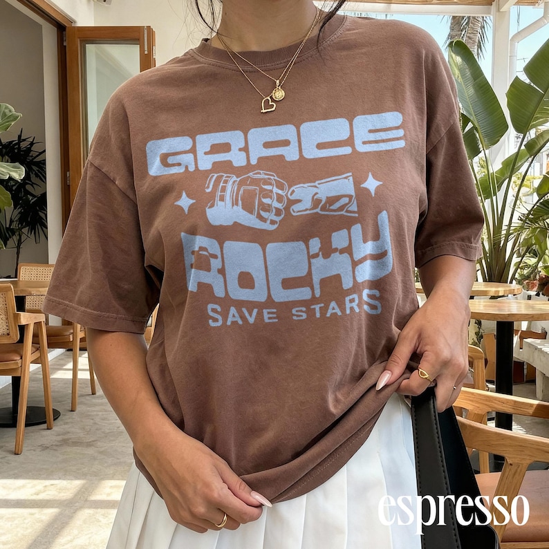 May include: Brown t-shirt with the text "GRACE ROCKY SAVE STARS" in light blue. The shirt features a graphic of boxing gloves and stars. The word "espresso" is printed in white at the bottom right.
