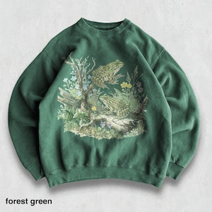 May include: Forest green sweatshirt featuring a detailed graphic of two frogs perched on a log amidst foliage and flowers. The design includes a tree branch and various plants. The text "forest green" is at the bottom.