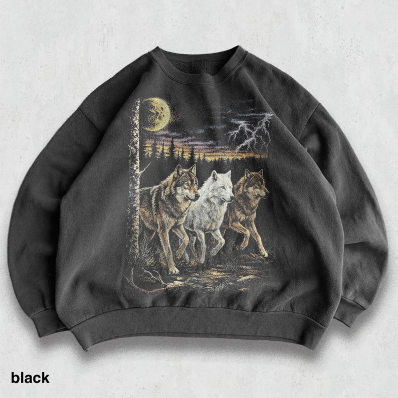 May include: Black sweatshirt featuring a graphic of three wolves running through a forest under a moonlit sky. The design includes a tree, lightning, and a color palette of black, brown, white, and yellow.