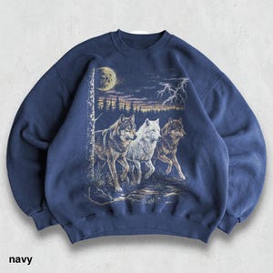 May include: Navy blue sweatshirt featuring a graphic of three wolves running through a forest under a moonlit sky with lightning. The text "navy" is printed at the bottom. The sweatshirt has a crew neck and long sleeves.