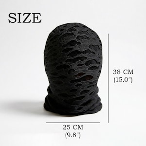 Op de afbeelding: Zwarte bivakmuts met een versleten, verscheurd ontwerp. De bivakmuts is 25 cm breed en 38 cm hoog. Het woord "SIZE" staat bovenaan gedrukt. Dit item is geschikt voor cosplay of mode.