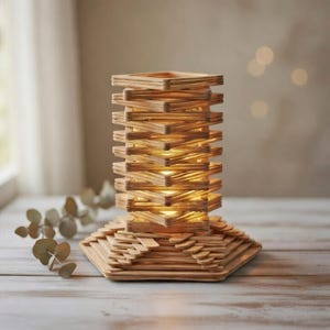 May include: A handmade wooden lamp with a unique design. The lamp is constructed from small wooden pieces arranged in a stacked, geometric pattern. The warm light shines through the gaps, creating a cozy ambiance. The lamp sits on a wooden surface.