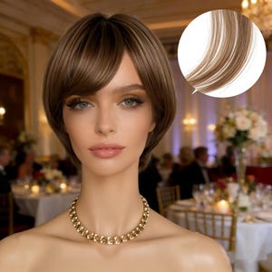 Puede incluir: Una mujer con cabello castaño corto y en capas con reflejos rubios y un flequillo lateral. Lleva un collar de cadena dorado. El fondo muestra un evento formal con mesas y personas.