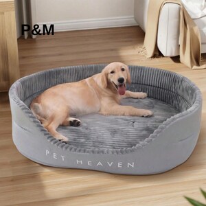 Puede incluir: Se muestra una cama redonda para perros de color gris claro con el texto "PET HEAVEN". Un golden retriever está acostado cómodamente dentro de la cama. La cama tiene una textura suave, similar a la pana, en el interior y un exterior liso.