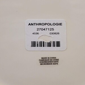 May include: A close-up of a white label with the word "ANTHROPOLOGIE" printed in black. Below the word are numbers and a barcode. The label also includes the text "MADE IN CHINA", "DISHWASHER SAFE", and "MICROWAVE SAFE".