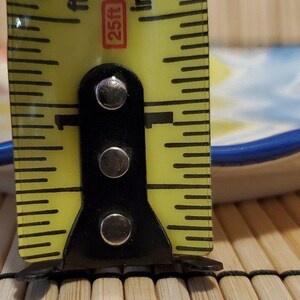 May include: A small, decorative ceramic dish with a wavy edge and a blue rim. The dish features a colorful, abstract design in shades of orange, yellow, and blue. The dish is approximately 1 inch in height.
