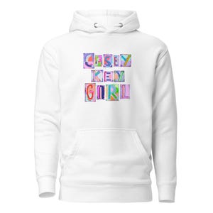 May include: A white hoodie with a front pocket and drawstring hood. The front features the text "CASEY KEY GIRL" in colorful, block letters. The letters are outlined in black and filled with various colors.