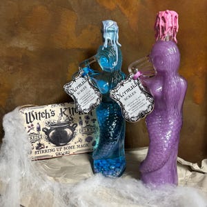 May include: Two mermaid-shaped glass bottles, one blue and one purple, with wax-sealed tops. The blue bottle contains blue beads. Each bottle has a tag that reads "Mermaid Scales". A box with the text "Witch's Kitchen" is also visible.