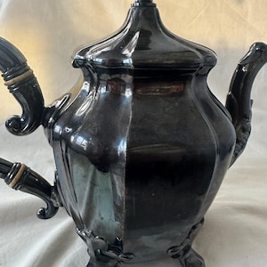 以下が含まれることがあります： 装飾的なデザインと3本の脚を持つ銀製のティーポット。ティーポットは、上にフィニアルが付いた蓋が付いています。ティーポットは銀製で、磨かれた仕上げになっています。