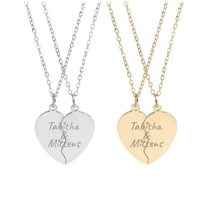 May include: Two necklaces with heart-shaped pendants, each split in half. One necklace is silver, the other gold. The pendants are engraved with the words "Tabitha & Mittens". The necklaces have delicate chain links.