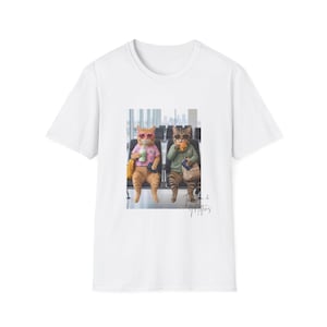 May include: White t-shirt featuring a graphic of two cats wearing sunglasses and sitting in an airport. One cat holds a drink, the other a sandwich. The text "Tabitha & Mittens" is below the image.
