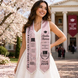 May include: A light pink graduation sash with the text "SOFTWARE ENGINEERING" and "Amelia Thomas". The sash features computer-related graphics, the University of California logo, and "Class of 2026".