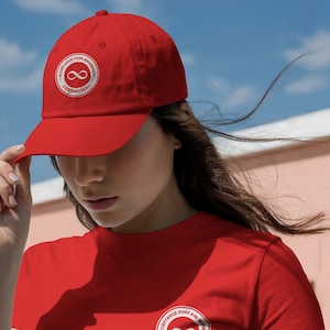 Puede incluir: Gorra de béisbol y camiseta rojas con un logotipo circular blanco que dice "Acceptance Over Awareness" y "#RedInstead" alrededor de un símbolo de infinito. La gorra la lleva una persona contra un fondo de cielo azul.